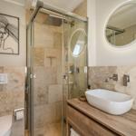 Badezimmer mit Dusche, Waschbecken und Toilette. Steinwand und runder Spiegel.