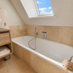 Bad mit Badewanne, Duschkopf und Dachfenster mit Blick auf den Himmel.