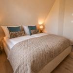 Schlafzimmer mit Bett, zwei Nachttischen und Lampen. Holzboden und weiße Wände.