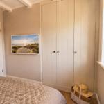 Schlafzimmer mit Bett, Kleiderschrank und Fenster. Wandbild zeigt Strand.