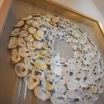 Gefärbtes Kunstwerk aus Muschelschalen in einem Holzrahmen an der Wand.