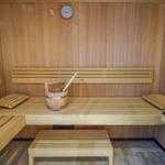 Sauna mit Holzbänken, Eimer und Thermometer an der Wand.
