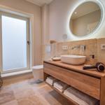 Badezimmer mit Waschtisch, Spiegel und Toilette. Fenster, Handtuchhalter und Bodenfliesen.