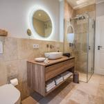 Badezimmer mit Waschbecken, Dusche und Toilette. Holzunterschrank und runder Spiegel.