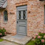 Haus mit Backsteinfassade, grauer Tür und Blumenbeeten