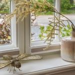 Auf dem Fensterbrett steht eine Vase mit Zweigen und eine geflochtene Libelle.