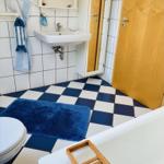 Badezimmer mit blau-weißem Fliesenboden, Waschbecken, Toilette und Badewanne.