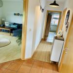 Flur mit Teppich, weißen Schrank und Tür zum Wohnzimmer mit Sofa und Couchtisch.