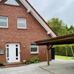 Rotes Backsteingebäude mit Eingangstür und Carport. Grünflächen und Satellitenschüssel sichtbar.