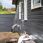 Outdoor shower on house wall with bench and towel.
