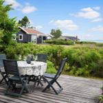 Wooden terrace with table and chairs, view of house and sea.
