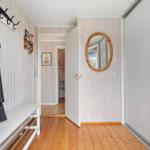 Hallway with wooden floor, coat rack, and round mirror on the wall.