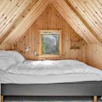 Attic room with wooden walls and ceiling, bed with white bedding and small window.