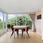 Dining room with wooden floor, glass walls, and brown chairs. Hanging lamp and glass cabinet.