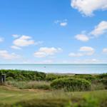 House with sea view and green meadows under blue sky with white clouds.
