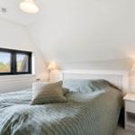 Schlafzimmer mit Bett, Nachttisch und Fenster mit Blick auf Grün.
