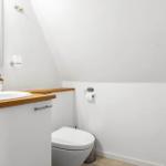 Badezimmer mit Waschbecken, Toilette und Spiegel an schräger Decke.