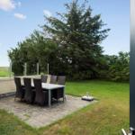 Terrasse mit Tisch und Stühlen, umgeben von Gras und Bäumen unter blauem Himmel.