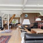 Wohnzimmer mit Kamin, Ledersofa und Holztisch. Helle Decke mit Balken. Terrasse im Hintergrund.