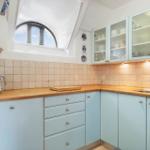 Küche mit hellblauen Schränken, Holzoberfläche und Badezimmerfenster.