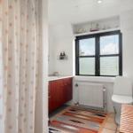 Badezimmer mit Fensterblick auf Wasser, Toilette, Holztisch und Badewannenvorhang.