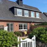 Haus mit Terrasse und Garten. Weiße Türen und Fenster. Schwarze Dachziegel.