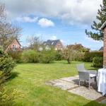 Garten mit Rasenfläche, Tisch und Stühle. Im Hintergrund sind Häuser und Bäume sichtbar.