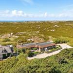 Haus mit Dach aus Stroh und moderner Terrasse in grüner Landschaft mit Blick aufs Meer.