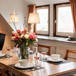 Esstisch mit Blumenarrangement und Gläsern vor Fenstern mit Holzrahmen.