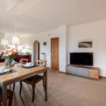 Essbereich mit Tisch und Stühlen, Wohnzimmer mit Fernseher und Schlafzimmer im Hintergrund.