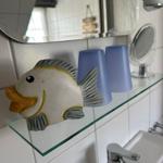 Bad mit Spiegel, Glasregal und Fischdekoration. Zwei blaue Gläser und Waschbecken mit Wasserhahn.