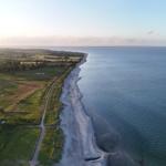 Aerielansicht einer Küstenlinie mit Strand, Grünflächen und ruhigem Wasser.