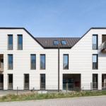 Moderne Mehrfamilienhaus mit Balkonen und Dachfenstern unter blauem Himmel.