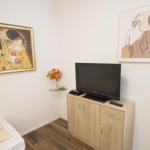 Zimmer mit TV, Schrank, Wandbildern und Blumenvase.