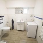 Badezimmer mit Dusche, Toilette, Waschbecken und Waschmaschine.