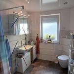 Badezimmer mit Dusche, Waschbecken und Toilette. Fenster mit Jalousie und Handtücher auf Regal.