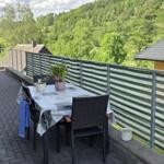 Terrasse mit Tisch, Stühlen und Blick auf grüne Hügel.