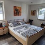 Schlafzimmer mit Doppelbett, zwei Fenstern und Holzmöbeln.