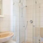 Badezimmer mit Dusche, Waschbecken und Toilette. Fliesenwand und Spiegel sichtbar.