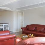 Wohnzimmer mit rotem Ledersofa, zwei Sesseln und Holztisch. Hintergrund zeigt Essbereich.