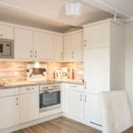 Küche mit weißen Schränken, Edelstahlgeräten und Holzoptik an der Wand.