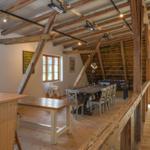Großer Raum mit Holzdecke, Tisch, Stühle und Fenster. Dachstuhl mit Strohdecke sichtbar.