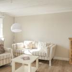 Wohnzimmer mit Sofa, Sessel, Tisch und Schrank. Fenster mit Rollladen. Holzboden und weiße Wände.