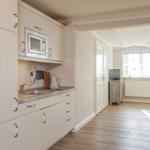Küche mit Mikrowelle, Spüle und Arbeitsplatte. Durchgang zu Wohnzimmer mit Fenster und Stuhl.