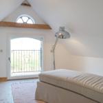 Schlafzimmer mit Dachschrägen, Fenster und Bett. Holzboden und Stehlampe.