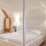 Schlafzimmer mit weißem Bett, Moskitonetz, zwei Nachttischen und Holzspiegel.