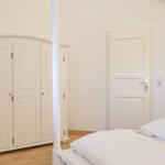 Schlafzimmer mit weißem Bett, Kleiderschrank und Tür