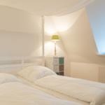 Schlafzimmer mit weißem Bett, Nachttisch und runder Fensteröffnung.