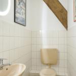 Badezimmer mit Toilette, Waschbecken und beleuchtetem Spiegel. Holzbalken an der Wand.