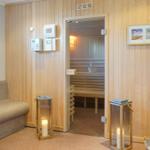 Sauna mit Holzwand und Sitzbänken. Vorraum mit Sofa, Kerzen und Pflanze.